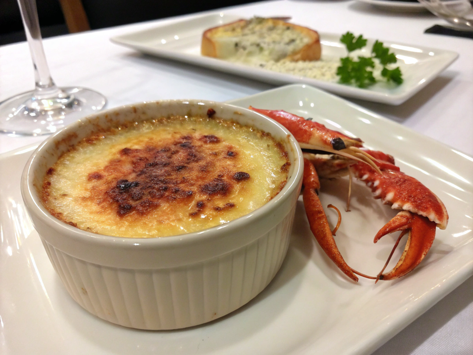 Golden crab brûlée in a ramekin, topped with caramelized sugar and garnished with chives, served on a rustic wooden board.