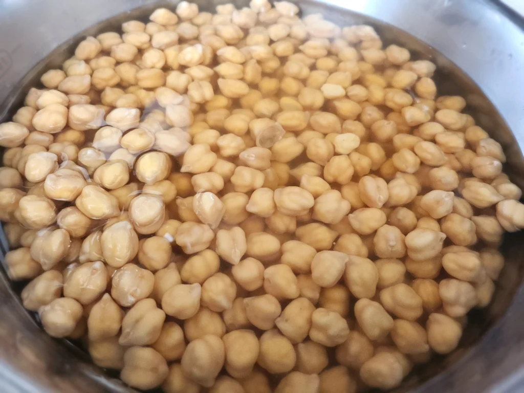 Soaked chickpeas in a stainless steel bowl, ready for cooking.

