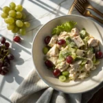 A refreshing bowl of chicken and grapes salad, made with tender chicken, juicy red and green grapes, crisp lettuce, and a creamy dressing, placed on a marble surface with soft natural light.