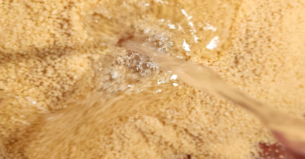 Water being poured over dry couscous, preparing it for cooking.