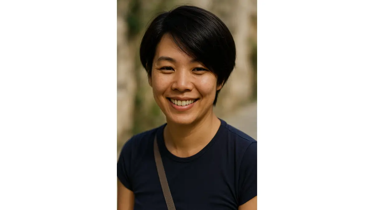 Saiko smiling in a close-up portrait with a soft stone wall background
