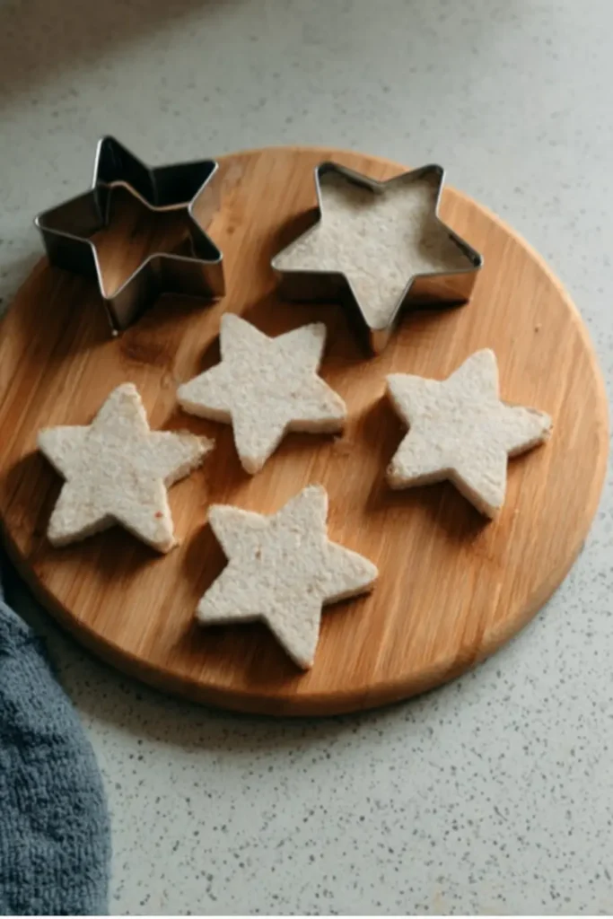 Elegant London-Inspired Cucumber Star Sandwiches Appetizer 3 Star-shaped bread pieces arranged on a bamboo cutting board next to metal star cutters for cucumber star sandwiches.
